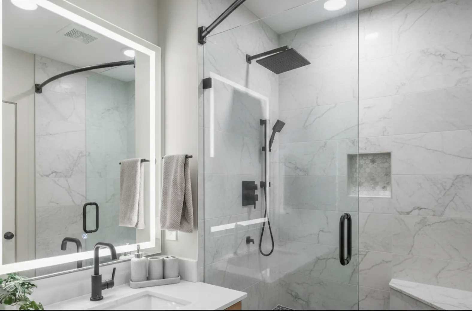 A Campus Gate bathroom with a glass walk-in shower and a lit mirror