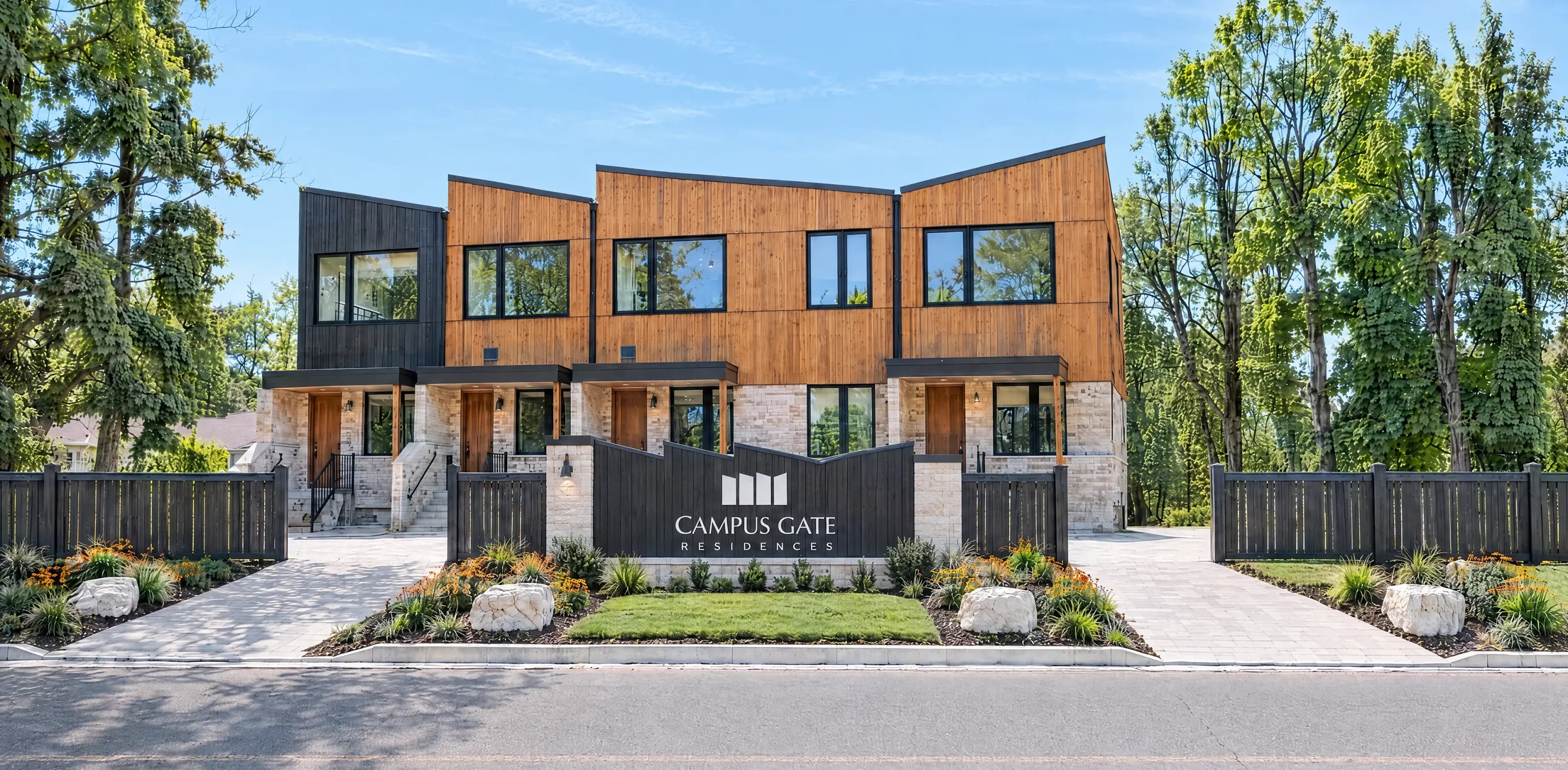 The Campus Gate residence from the street: timber-clad townhouses behind a dark fence and the Campus Gate entrance sign