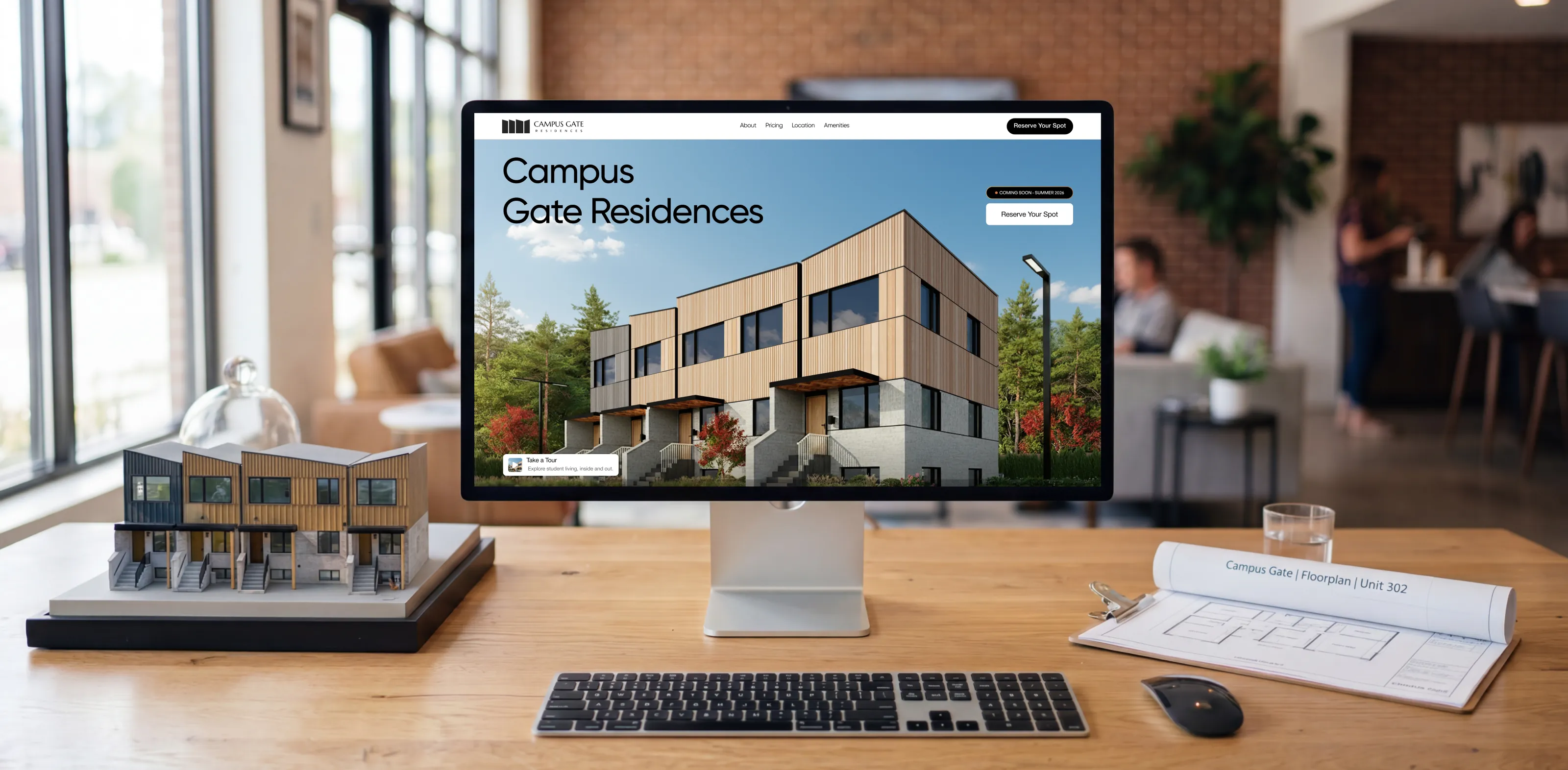 The new Campus Gate website on a desktop monitor, beside a scale model of the residence and a rolled-up floor plan
